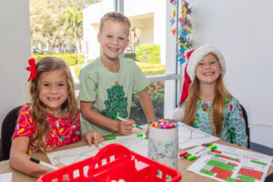 Girl, boy, and girl wearing holiday clothes, creating crafts in VBMA art studio